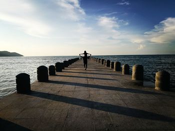 Rear view of father giving piggyback to daughter amidst sea on pier