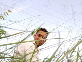 Low angle view of man seen through grass against sky