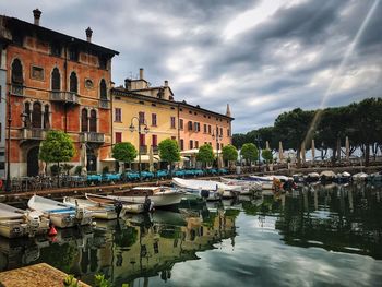 Boats moored in canal by buildings against sky in city