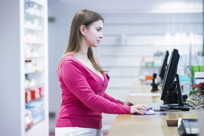 Pharmacist working on desktop pc at counter in pharmacy