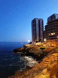 Illuminated buildings by sea against clear blue sky