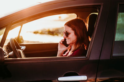 Woman sitting in car and using smartphone