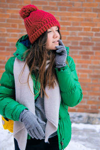 Young woman wearing hat standing against snow during winter