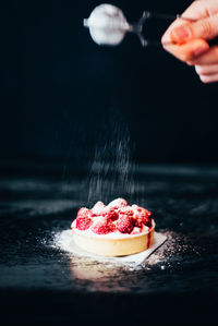 Woman sprinkling powdered sugar on tart at table