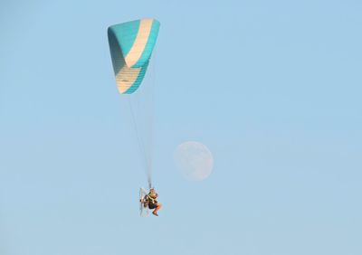 Low angle view of man paragliding against clear blue sky