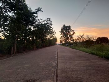 Empty road amidst trees against sky at sunset