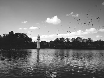 Silhouette birds flying over river against sky