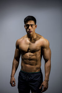 Portrait of shirtless muscular man standing against wall