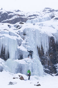 People climbing snow covered mountain during snowfall