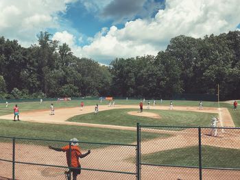 Group of people playing baseball on field against trees