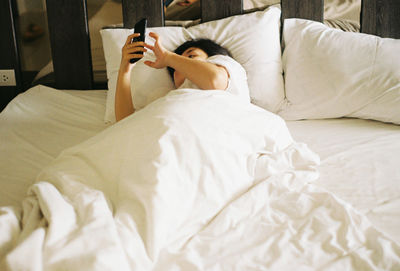 High angle view of woman using phone while lying on bed at home