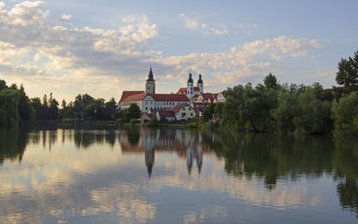 Building by lake amidst trees against cloudy sky during sunset