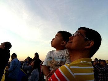 Father carrying son against sky during sunset