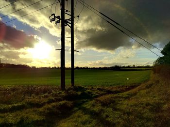 Electricity pylon on grassy field against cloudy sky