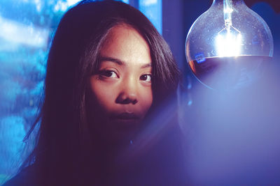 Close-up portrait of smiling woman by light bulb in darkroom