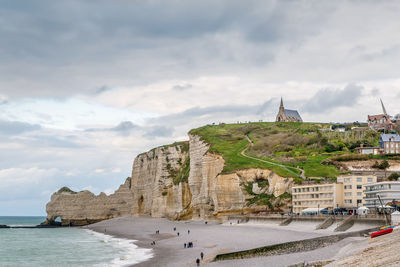 Buildings by sea against cloudy sky