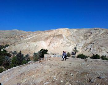 Man walking on arid landscape against clear blue sky