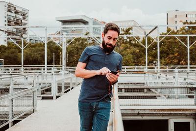 Young man using mobile phone while standing against buildings