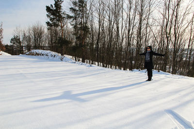 Woman with arms outstretched standing on snow covered field against bare trees