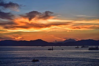 Silhouette boats on sea against orange sky