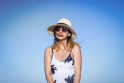 Portrait of pregnant woman in sunglasses and hat against clear blue sky