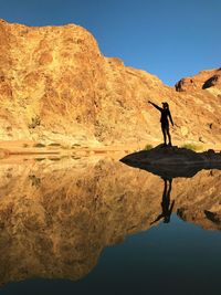 Young woman pointing while standing on rock in lake against sky