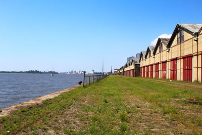 Buildings by sea against clear blue sky