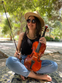 Portrait of smiling young woman wearing sunglasses sitting outdoors and violin in hand