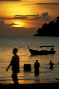 Silhouette people in sea against sky during sunset