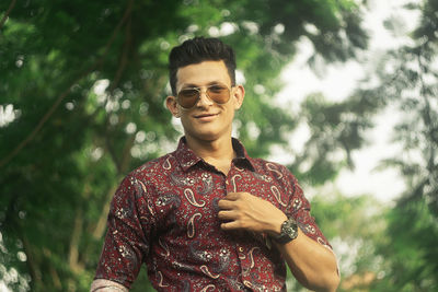 Portrait of young man wearing sunglasses standing against plants