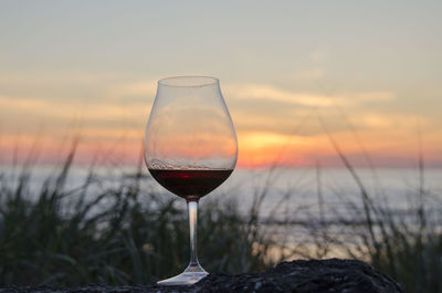 Close-up of wineglass against sky during sunset