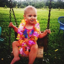 Cute baby girl wearing floral garland sitting on swing in park