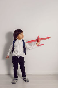 Boy child in a white shirt and jeans flies on a red airplane toy at the white wall of the house