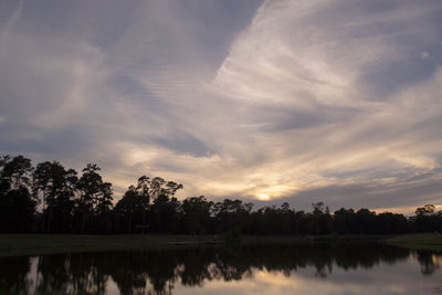 Reflection of silhouette trees in calm lake at sunset