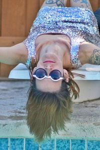 Portrait of young woman wearing sunglasses and shiny dress while lying on poolside