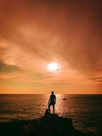 Silhouette man standing on sea against sky during sunset