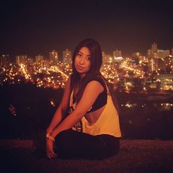 Portrait of woman sitting on illuminated city at night