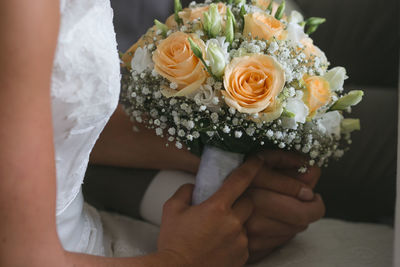 Midsection of bride and groom holding rose bouquet