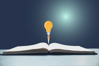 Digital composite image of light bulb over open book on table