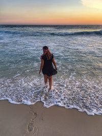 Rear view of woman walking at beach during sunset