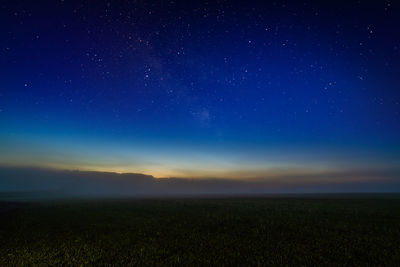 Scenic view of foggy night field against starry dark blur sky