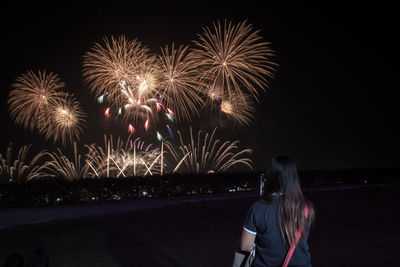 Rear view of woman with firework display at night