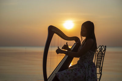 Woman playing musical instrument at beach during sunset