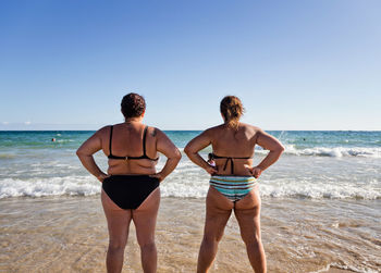 Rear view of friends standing on beach against clear sky