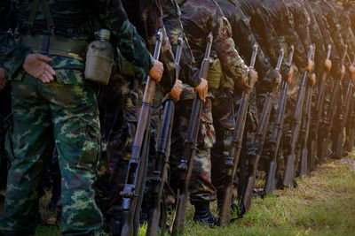 Low section of army soldiers with guns standing in row on field