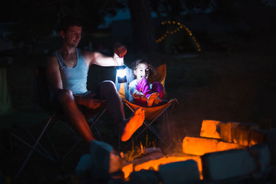 Father and daughter camping by bonfire at night