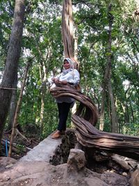 Woman sitting on tree trunk amidst plants in forest