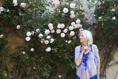 Smiling senior woman standing against flowers blooming in park