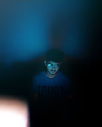 Portrait of young man standing against dark wall