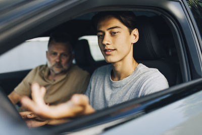 Young man getting driving lessons from father while sitting in car